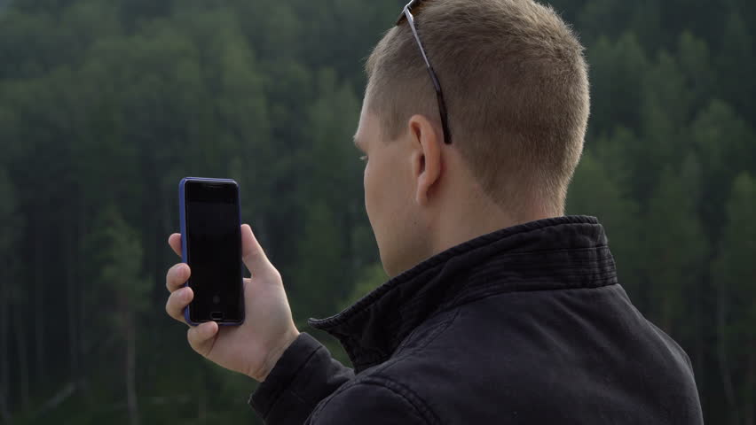 Young tourist man with smart cell phone taking picture selfie of amazing nature