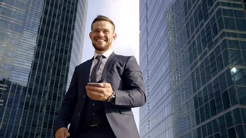 young manager is wearing three-piece suit is talking by phone, standing in background skyscrapers