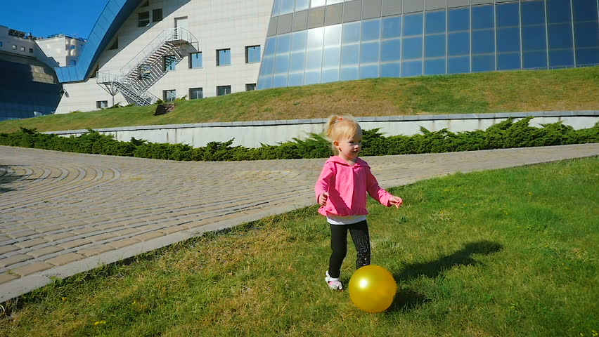 SLOW MOTION: girl of three-years jumps on a rubber ball on a lawn.