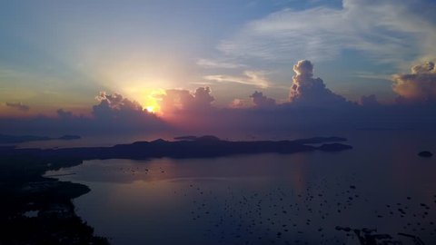 Dramatic sunrise at eastern coast of Phuket island, over Chalong bay and Panwa cape. Dark cumulus clouds towering at horizon, bright sun beam shine from behind. Shaded land stripe stretched into sea