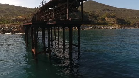 Aerial, rise up from sea level next to old conveyor belt bridge from mining Era on Elba
