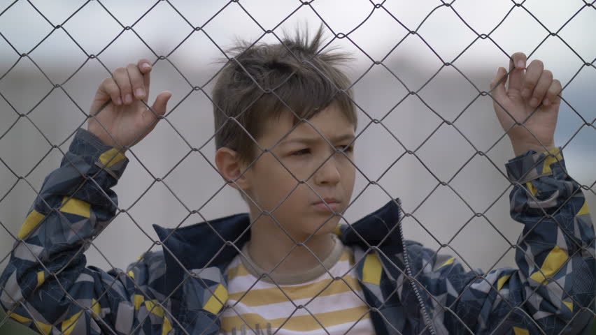 serious disappointed boy behind an iron fence looks into the camera and lowers his eyes down, regret for the deed Royalty-Free Stock Footage #30784702