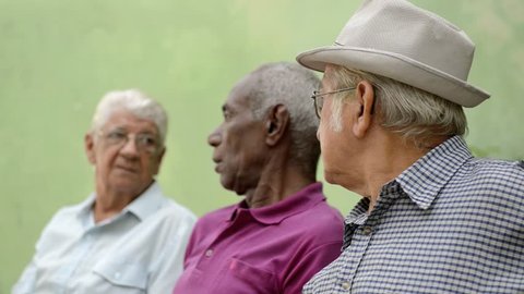 Active retirement and senior people, group of three old male friends talking and laughing on bench in public park. Sequence Stock Video