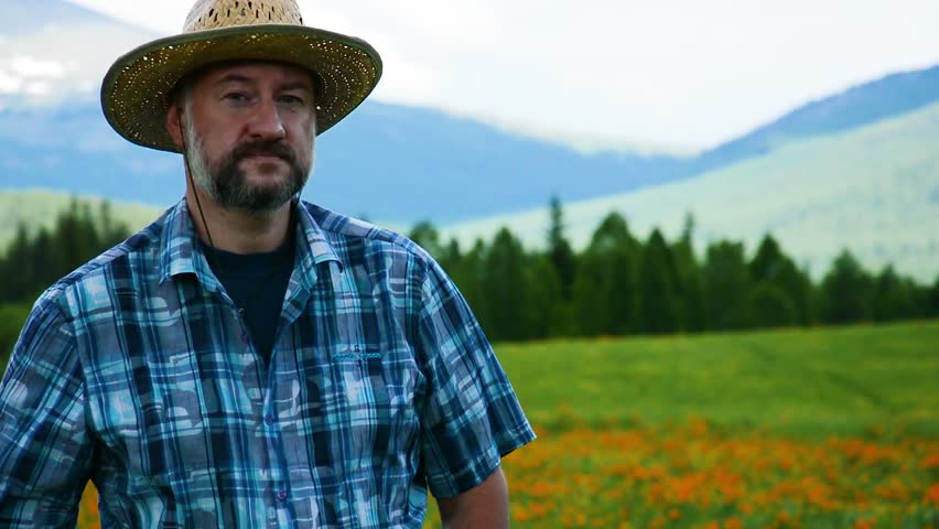 Man farmer in a straw hat on a background of a high-mountain field with flowers. In the background is the cedar forest, the cloudy sky. Royalty-Free Stock Footage #30788422