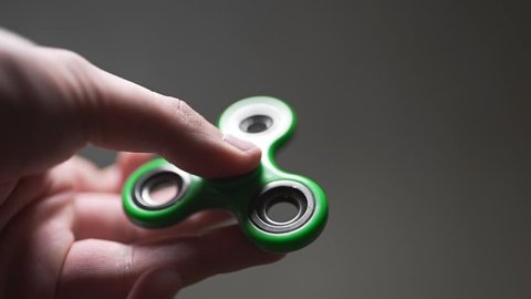 Man twists green spinner in his hand, fidget spinner is twisting round and round, toys for everyone
