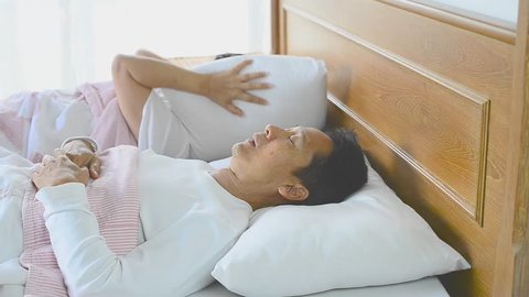 Snoring man choking out loud waking his wife up during the noisy night and she close ears with pillow.
Obstructive sleep apnea symptoms .
 