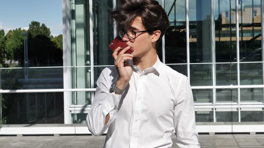 Handsome trendy man wearing white shirt standing and recording voice message on cell phone that he is holding, outdoor in city setting | Shutterstock HD Video #30797842