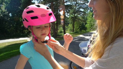 Caring young mother puts safety helmet on his little daughter's head. Slow motion