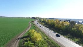 The car is going on the road through the field aerial view. Footage. Cars goes on the sunlit road through fields and forests. View from the side of the road
