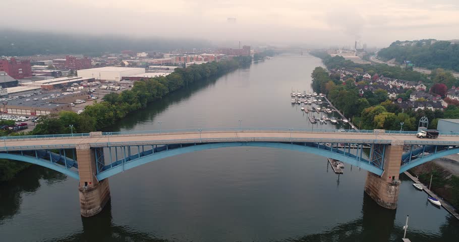 An early morning wide profile aerial establishing shot of traffic passing over the 31st Street Bridge with the foggy Pittsburgh skyline in the distance.  	