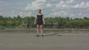 Sporty woman exercising with barbell over city waterside background
