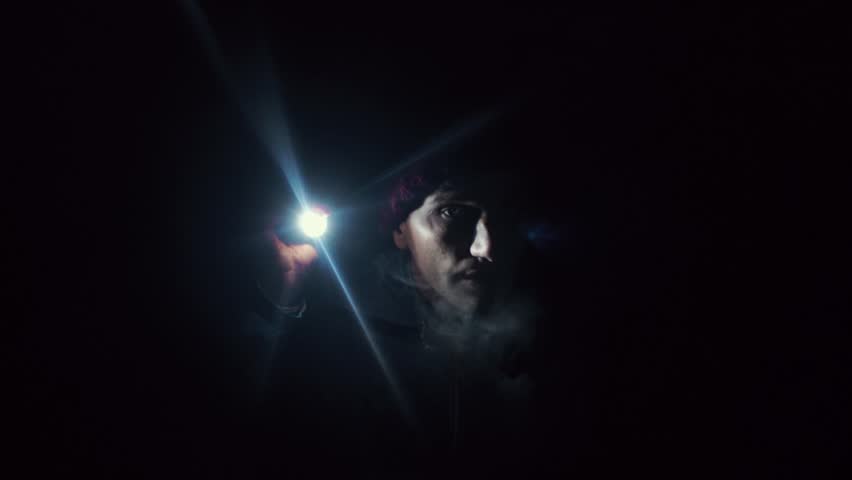 Young man standing in deep darkness place illuminates the darkness with flashlight. Steam comes from the mouth. Royalty-Free Stock Footage #30812848