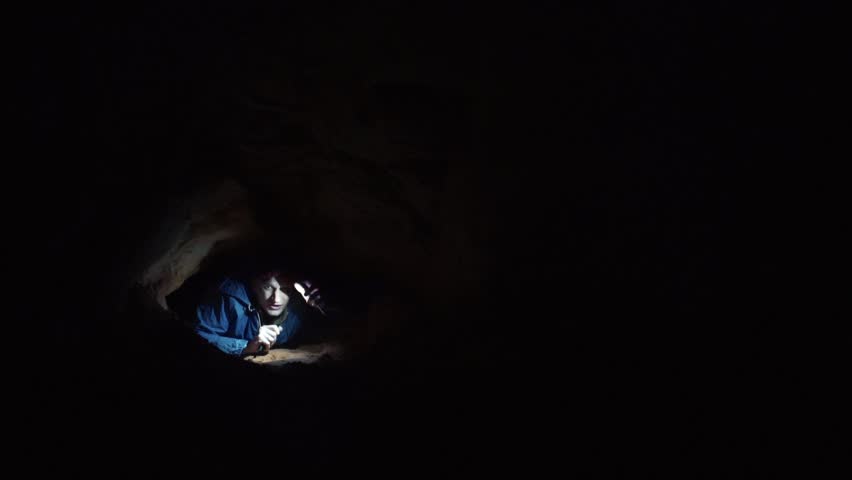Young man scrambles out from a narrow hole inside the cave illuminates the way with flashlight in his smartphone. Absolutely deep darkness around. Royalty-Free Stock Footage #30812890
