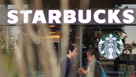 Burnaby, BC, Canada - September 14, 2017 : Slow motion of people walking through starbucks store with blurry leaves blowing in front of camera