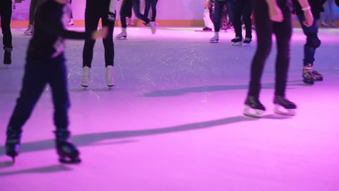 Close-up view of men and women feet. Crowd skating on the ice with colored light together, enjoying the leisure.