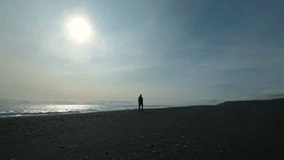 Young man walking on a black sandy beach on a mountain. During vacation the man is in warm clothes. A person is on the shore of a walk