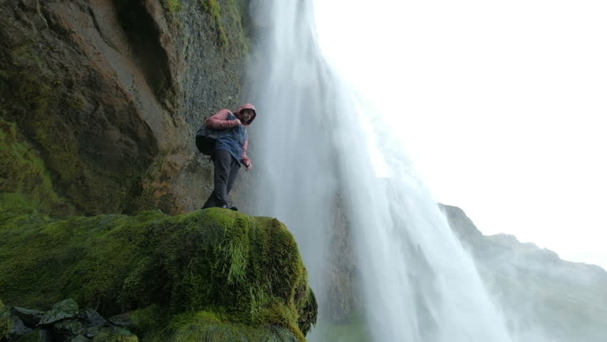 Tourist man in a red jacket stands and looks at a stream of falling water. Beauty in nature