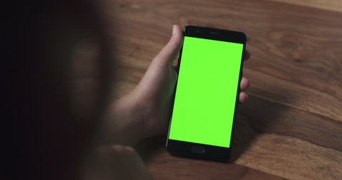 handheld shot of female teen girl using smartphone with green screen over wood table