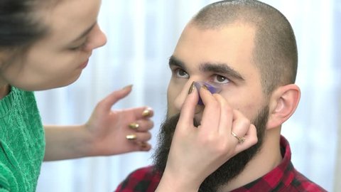 Bearded man getting makeup. Visagist using sponge, foundation.