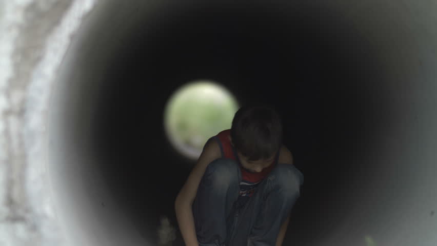 Sad teenager boy sitting alone hiding inside of a drainage tunnel, lonely homeless boy, refugee