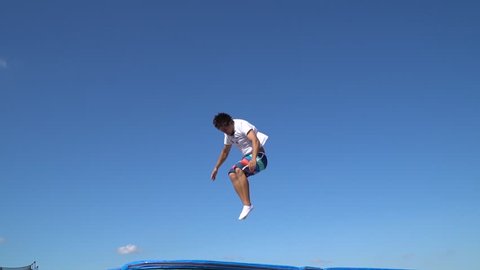 Adult man in beach shorts shows acrobatic stunts on a trampoline, slow motion