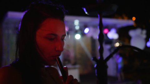 sexy young woman smoke a hookah on party at night club into blue lights in slow motion, close-up  