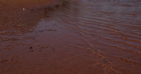 Water coming in on red sand beach - slow motion - tilt up