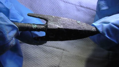 Archeologist inspects authentic ancient arrow head made of metal, colored