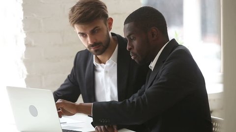 African american businessman showing computer presentation to caucasian client sitting at office desk, explaining new project business plan with pc at meeting, diverse partners negotiate using laptop