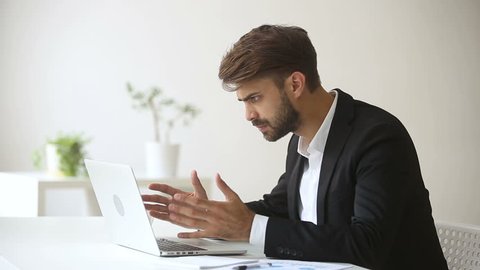 Annoyed angry businessman troubled with sudden computer failure, stressed man having problem with broken pc using laptop, pressing keys on hanging device, leaving workplace unable to fix gadget