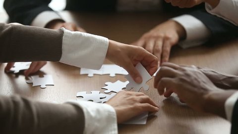 Close up view of business people hands trying to connect assembling jigsaw puzzle and join pieces on conference table in office, team help and support, finding right solutions in teamwork concept