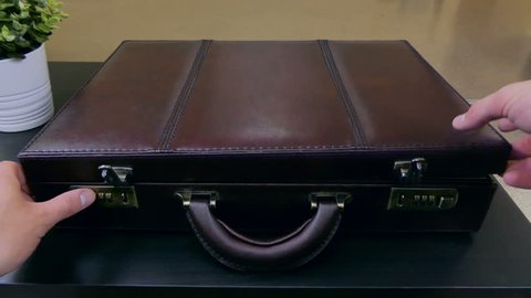 A businessman opens a leather case with a combination lock with documents inside on his desk. Case is trimmed with red leather