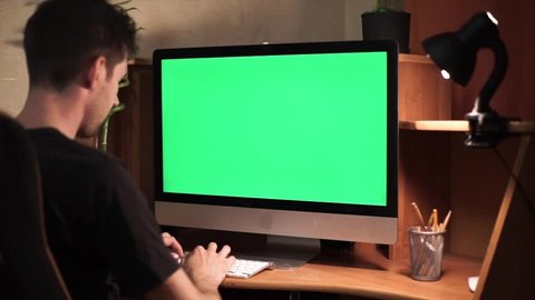 A man types on a laptop on his desk. Green screen for your custom screen content.