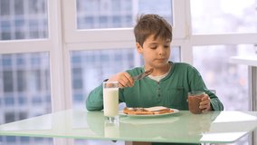 Boy child preparing chocolate hazelnut spread toast HD slow-motion video. Kid morning breakfast of cocoa sweet paste on bread with milk