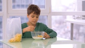 Boy child eating cereal cornflakes from bowl HD slow-motion video. Kid morning breakfast of corn flakes and milk. 