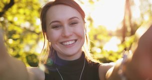 Portrait of a Beautiful Young Woman Having Video Chat Outdoors. SLOW MOTION 4K DCi. Attractive Happy Girl looking to camera, laughing, talking, smiling. Sunny park background with Lens Flare.