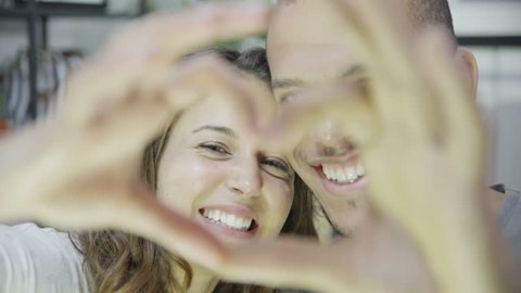 Close up of an attractive young mixed ethnicity couple who are laughing and making a heart shape with their hands. In slow motion.: film stockowy