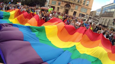 PRAGUE, CZECH REPUBLIC AUGUST 12, 2017: GLBT guys and girls wave rainbow flag at Gay Pride parade. Cheerful girls smiling and waving their hands at camera. Symbol of gay, lesbian, bisexual community.