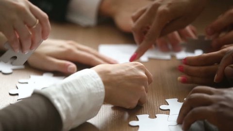 Close up view of hands assembling jigsaw puzzle on table, group of business people matching pieces playing board game, right decision making in business, help and support in teamwork concept