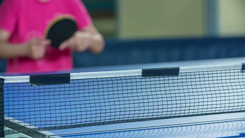 A yellow ping pong ball is travelling from one side of the table to another side. Girls are playing table tennis in school.
