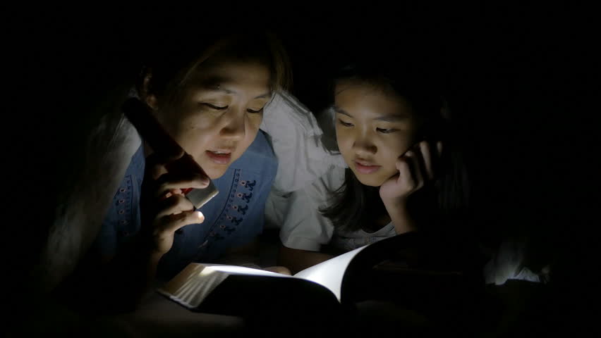 4K : Asian mother reading a scary tales to her daughter  with flashlight under the sheet