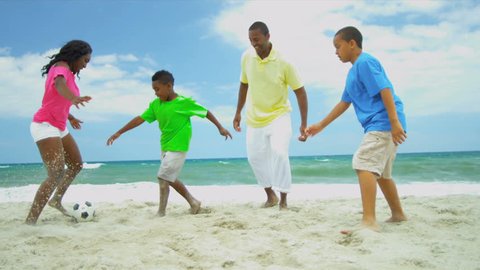 Football game of ethnic father wit young sons and teenage daughter on beach