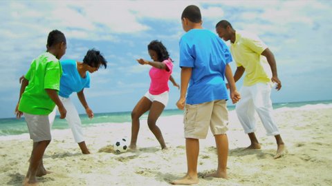 African American family spending summer kicking soccer ball on beach