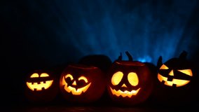 Halloween pumpkins in a row with candles, blue light rays and smoke with human hands silhouette at background, front view