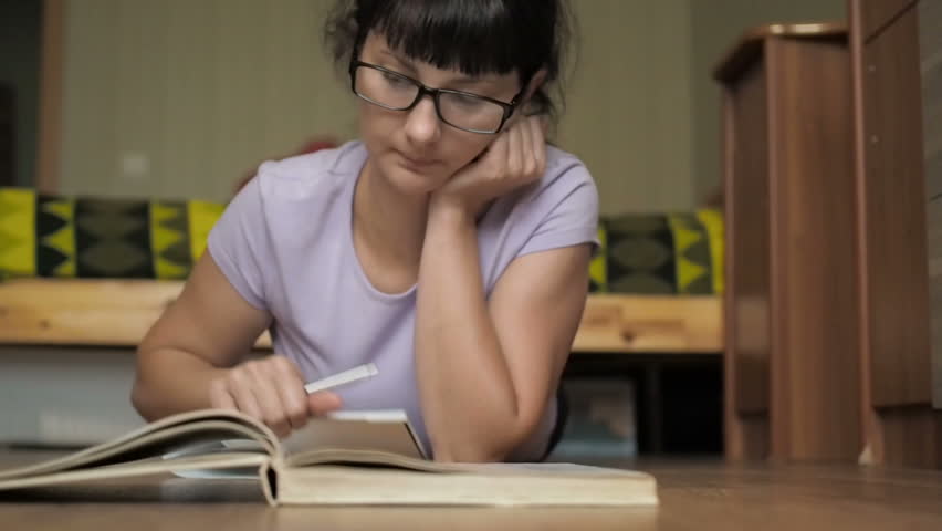 Student girl studying writing in notebook . Beautiful college student girl laying on floor studying writing in notebook. Young woman with glasses his books and tablets.