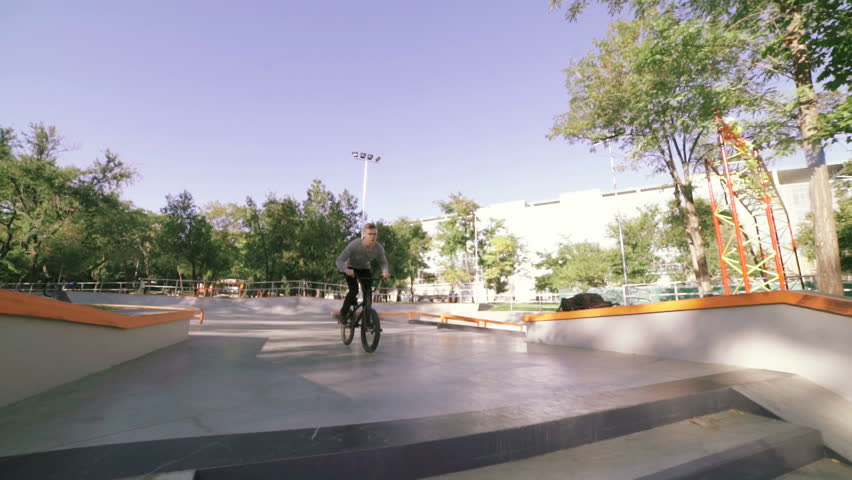 BMX rider doing tricks in extreme park during sunset, slow motion