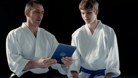 Martial Arts Master Wearing Hakamas Teaches Young Student Aikido Tecnique with the Help of the Tablet Computer. Shot Isolated on Black Background and in Slow Motion. Shot on RED EPIC-W 8K Helium.