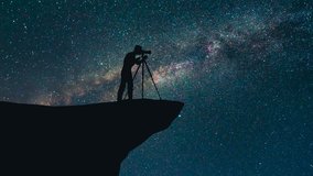 The man with a camera stand on the mountain against a sky with stars. time lapse
