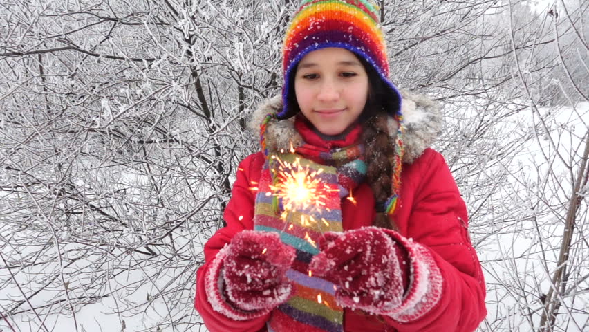 Happy girl in warm clothes with burning sparlkes on winter forest landscape, slow motion 