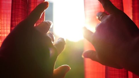 The girl opens red curtains and played with his hands through the sun's rays. Hand closeup